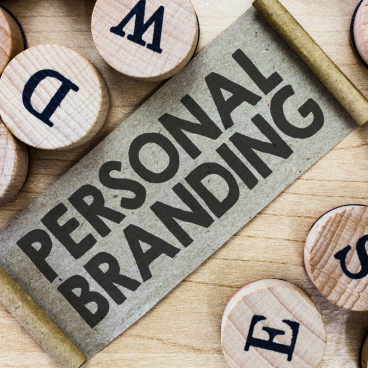 Wooden blocks with letters surrounding a scroll with the words 'Personal Branding' written on it, placed on a wooden surface